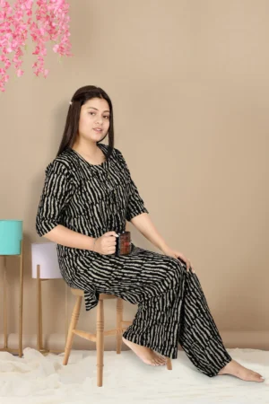 Product: Alpine Kurti Palazzo Black Night Suit. A women sitting on a stool wearing the product.